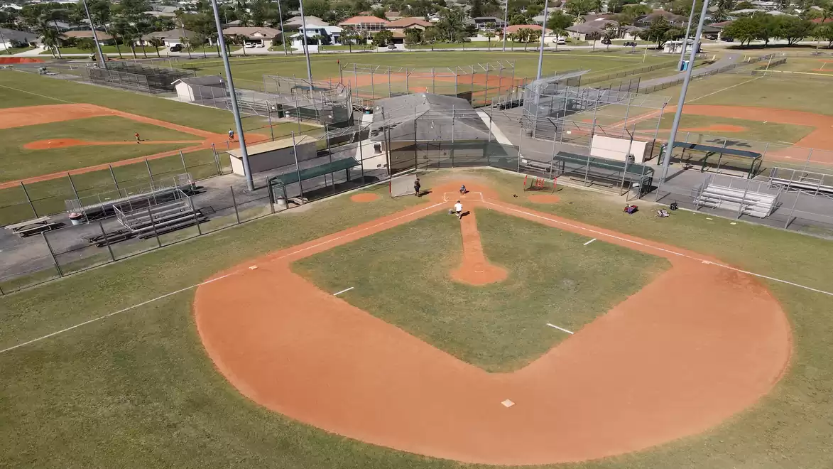 Aerial view of a well-maintained baseball field with surrounding spectator stands and additional fields in the background.