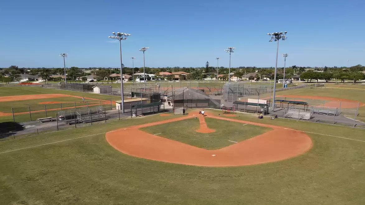 Aerial view of an empty baseball field with orange-brown dirt and green grass on a sunny day.