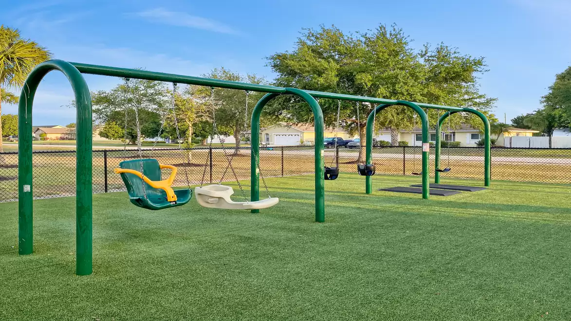 A children's playground with swings on green grass under a blue sky.