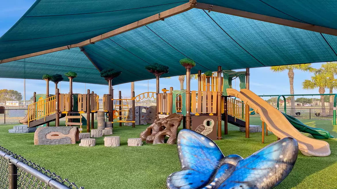 A covered playground with climbing frames, slides, and a large blue butterfly in the foreground.