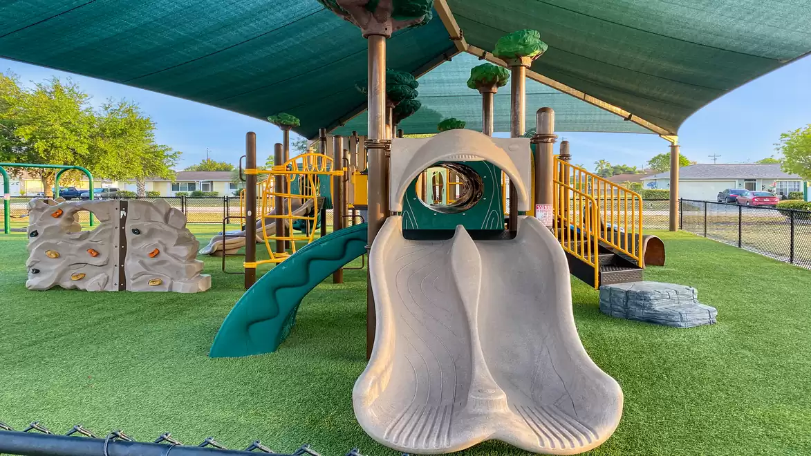 A modern playground with a climbing wall, slide, and covered area on green artificial grass.