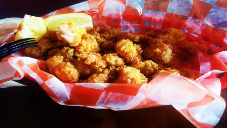 Basket of breaded and fried alligator meat on red and white checkered paper, served with a lemon wedge.