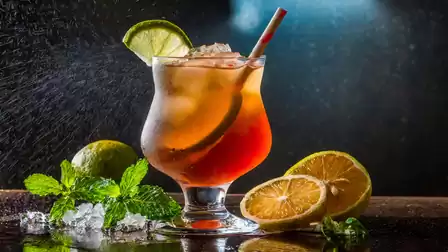 A refreshing cocktail with ice cubes in a glass, garnished with lime and mint, photographed against a dark background.