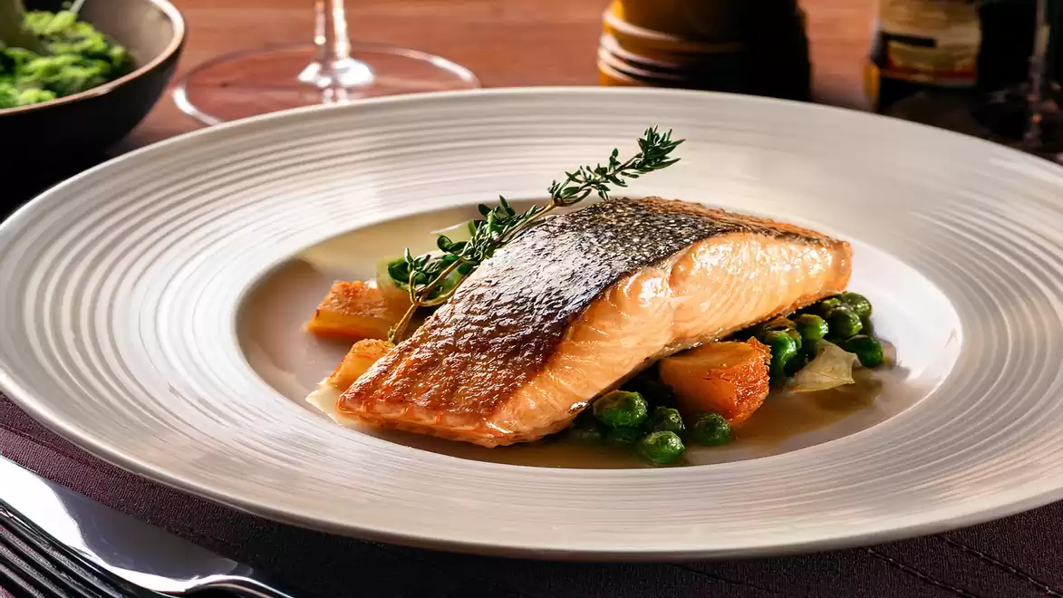 A plate with a seared salmon fillet on a bed of green peas and diced potatoes, garnished with fresh herbs.