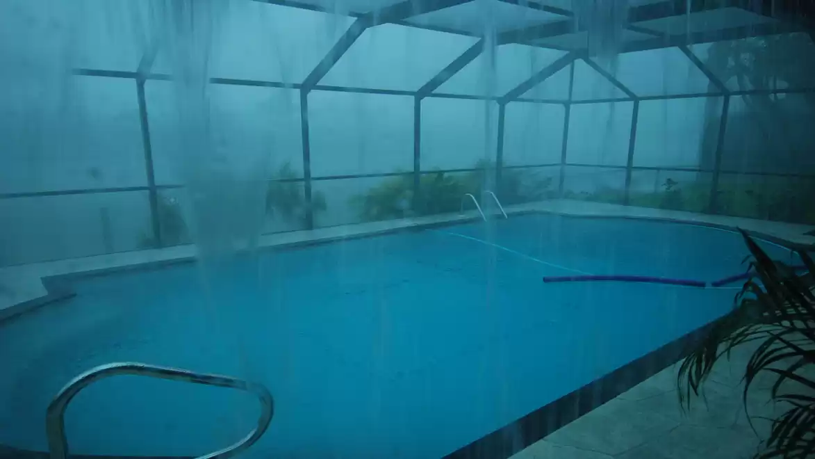 An indoor pool area during heavy rain. Water drips from the ceiling, and plants are visible at the edge of the pool.