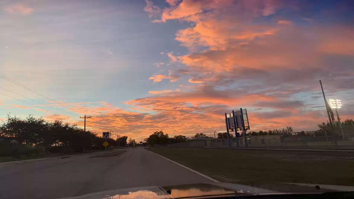 A country road at sunset with dramatic orange clouds in the sky.