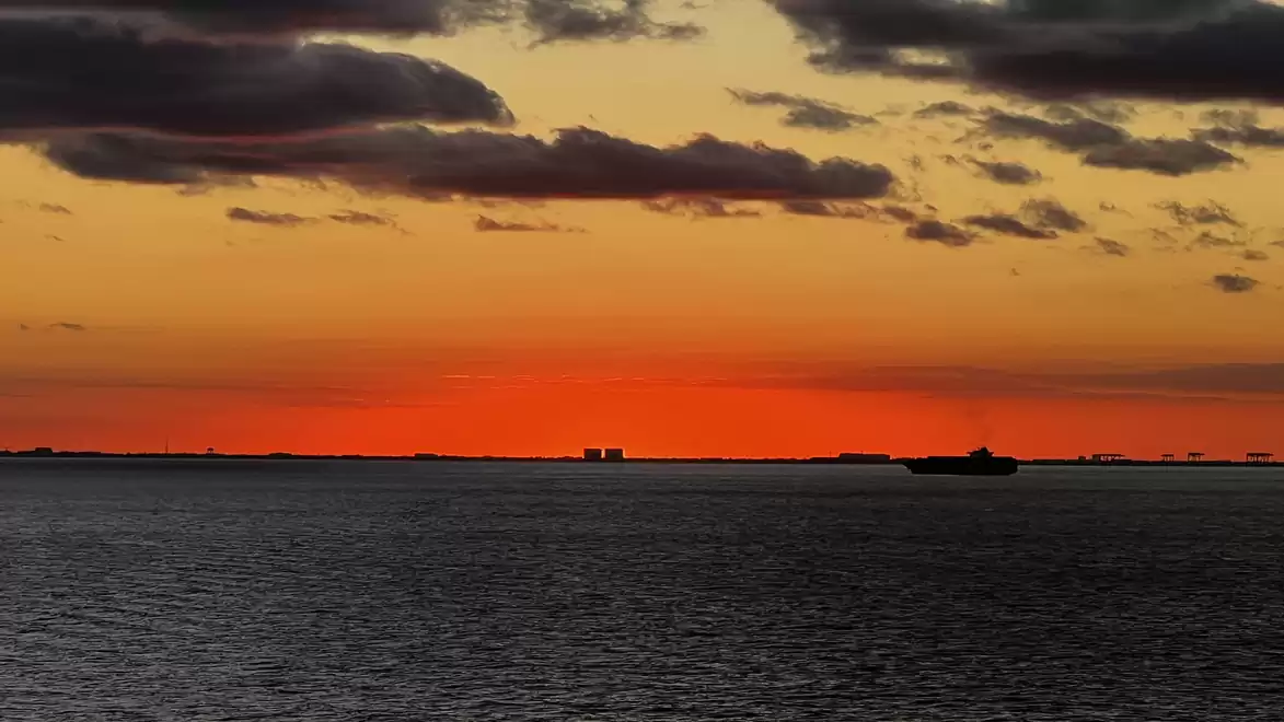 Dramatic sunset over the sea with clouds in the sky and a ship on the horizon.