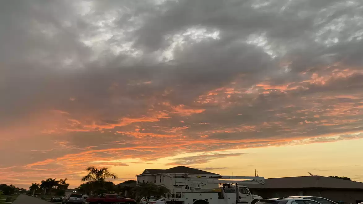 Dramatic sky with red-lit clouds during sunset over suburban houses with palm trees.
