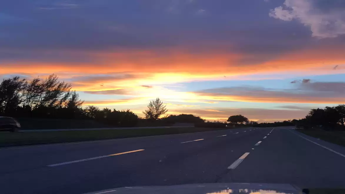 Highway at sunset with dramatic sky and orange-blue clouds.