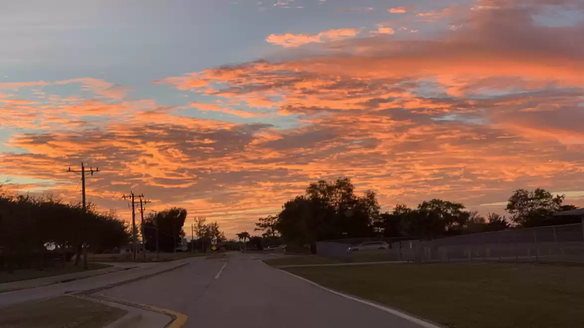Road at sunset with dramatic sky and clouds in shades of orange and pink.