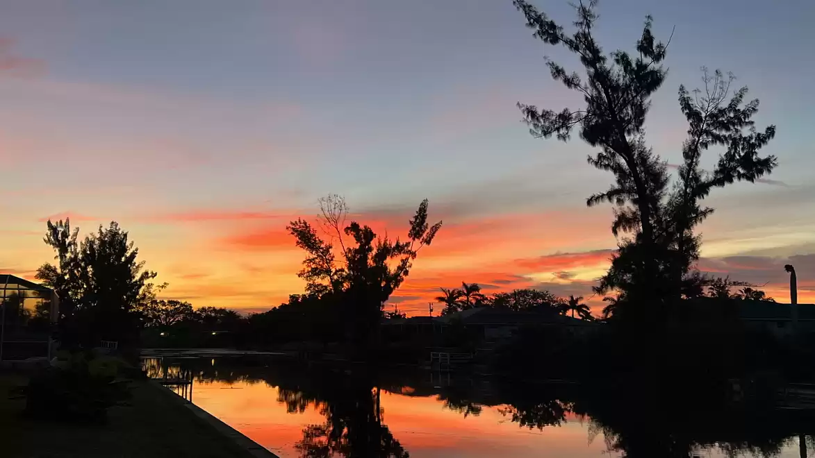 Sunset over a tranquil lake with silhouettes of trees and a colorful sky.