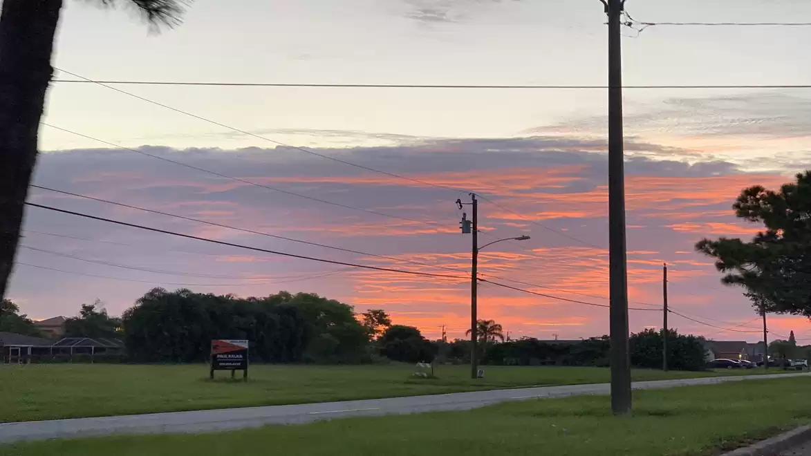 Sunset with orange sky and clouds, utility poles and trees on the horizon