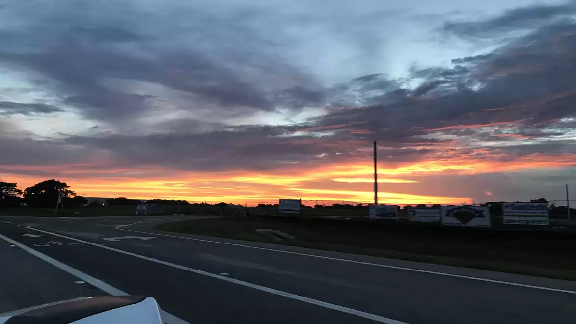 A picturesque sunset over a quiet country road with dramatic cloud formations in the sky.