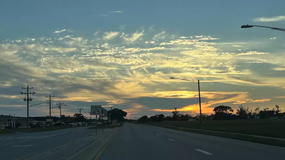 Road at sunset with a slightly cloudy sky and trees on the horizon.