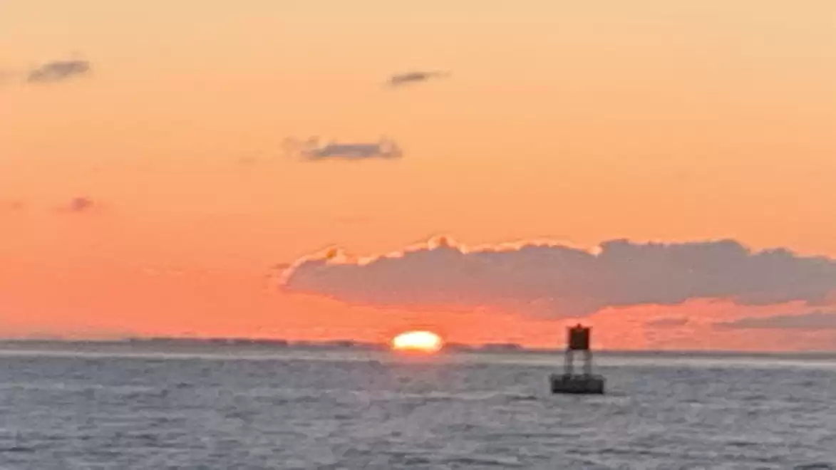 A sunset over the sea with a boat in the distance and orange clouds on the horizon.