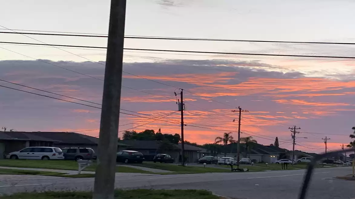 An urban neighborhood at sunset with orange clouds and power lines.