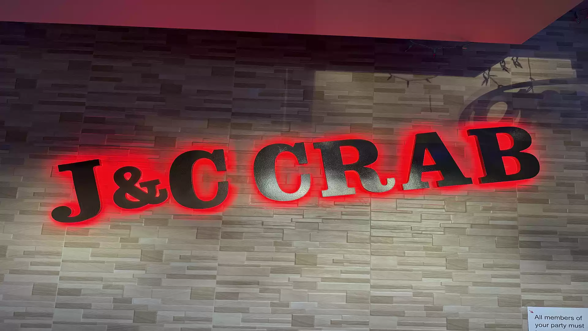 Neon sign of J&C Crab on a brick wall.