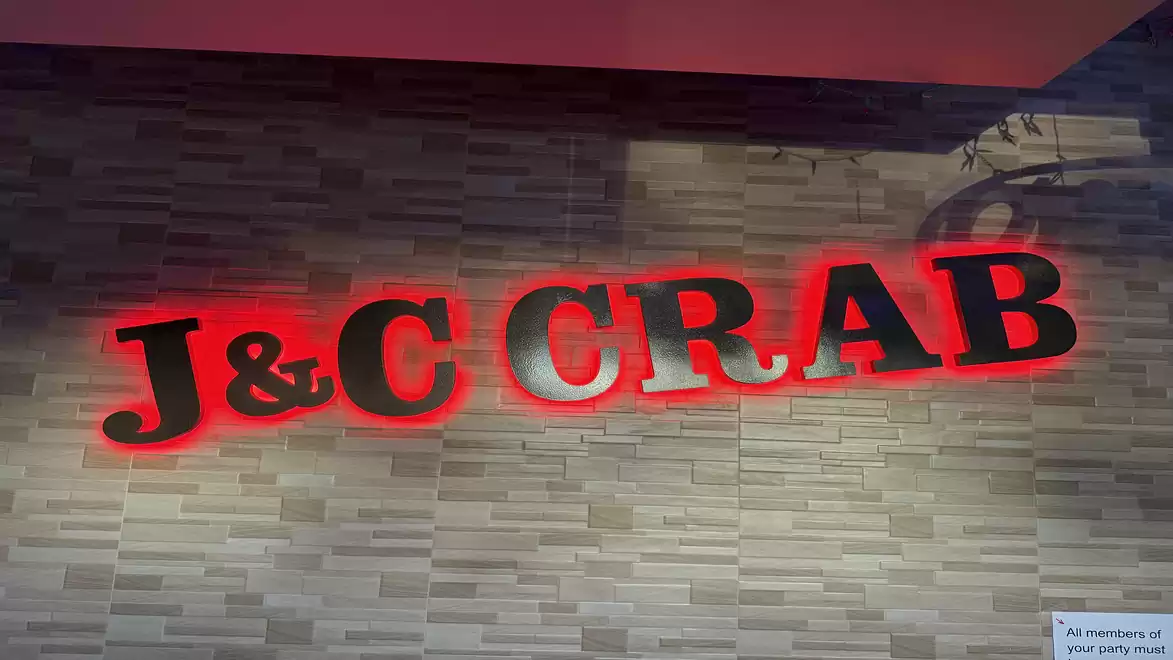 Neon sign of J&C Crab on a brick wall.