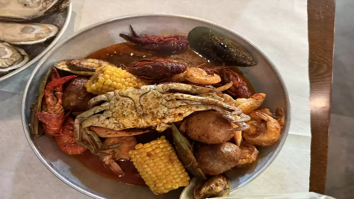 A plate containing a variety of seafood, including crabs, shrimp, and mussels, surrounded by corn cobs and potatoes, served with a spicy sauce.