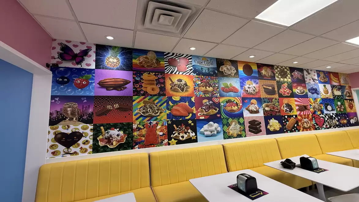 A cafe with colorful wall decorations featuring various chocolate designs, yellow benches, and a white table in the foreground.