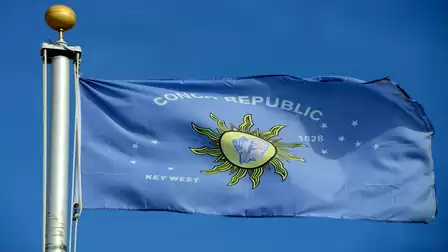 Blue and white Conch Republic flag with sun logo, waving in the wind against a clear sky.