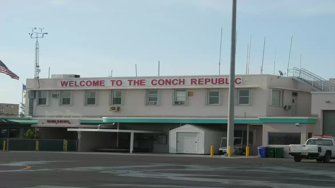 Building with the sign 'Welcome to the Conch Republic' in a harbor area under a cloudy sky.