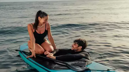 A man and a woman enjoying a relaxed time on a surfboard in the sea. The woman sits on the board while the man leans in the water.
