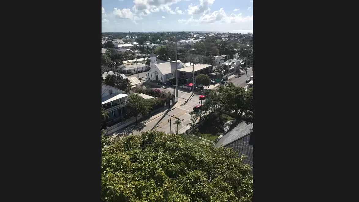 Aerial view of an urban scene with white buildings and green vegetation under a blue sky with clouds.