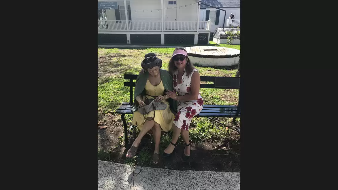 Two women sitting on a bench outdoors, smiling and wearing summer clothing.
