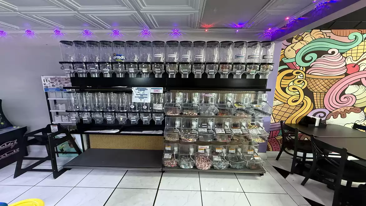 A self-service shop with a wall full of acrylic dispensers for cereals and candies, arranged side by side. To the right is a colorful wall sticker featuring ice cream cone motifs.