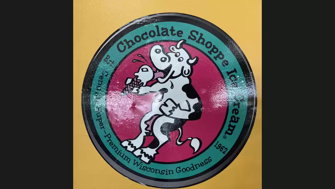 Logo of Chocolate Shoppe Ice Cream featuring a cartoon cow holding an ice cream on a yellow background.