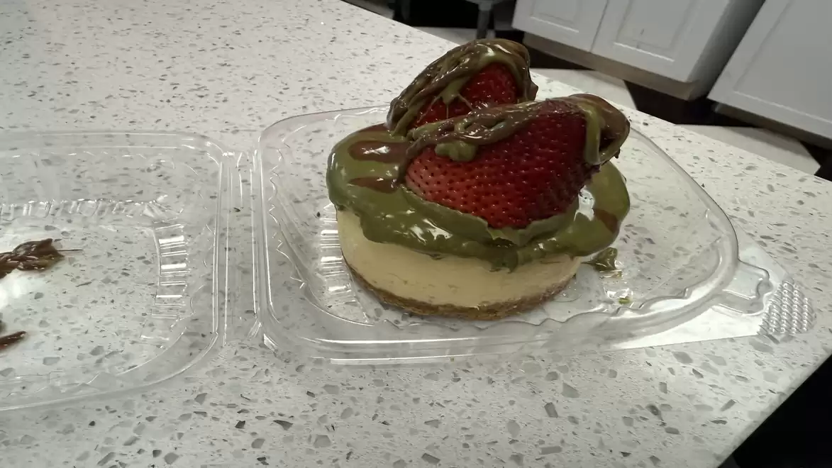A dessert on a light plate with two large strawberries covered in a green cream and dark sauce.