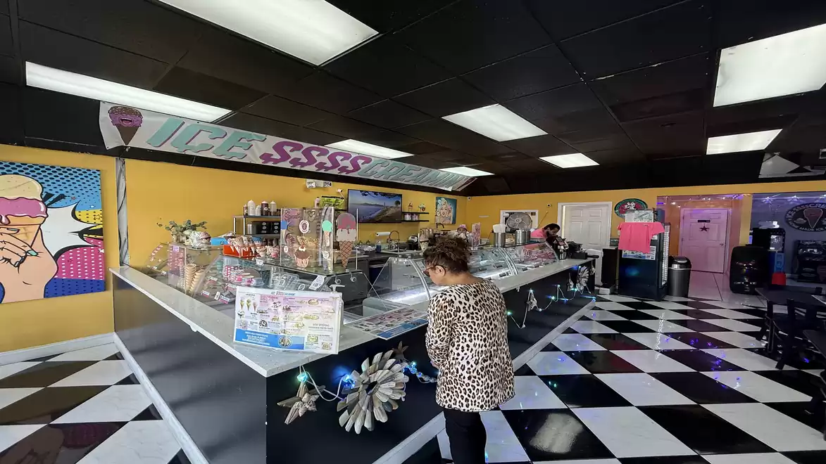 A modern ice cream parlor with a checkered floor and a woman selecting ice cream in a leopard print Shirt.