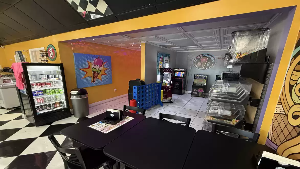 Interior view of a modern restaurant with colorful walls, black tables, and a black and white tiled floor. A fridge with drinks and a wall with pop-art graffiti are visible.