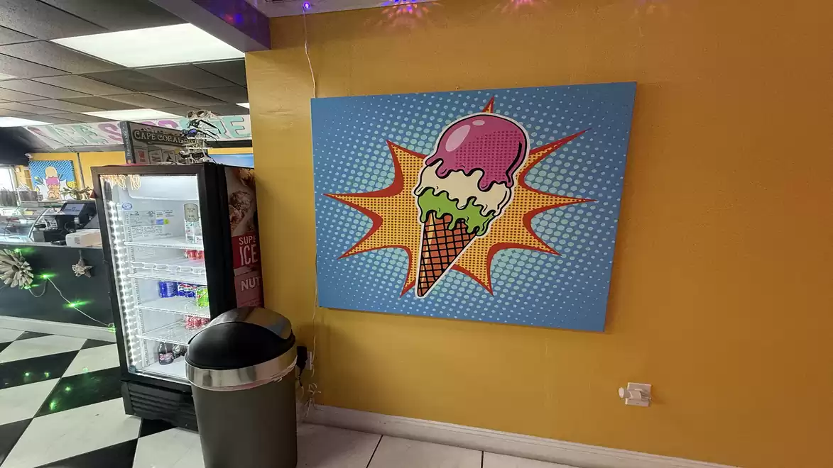 A pop art style wall painting of an ice cream with three scoops on a yellow wall next to a refrigerator in an ice cream shop.