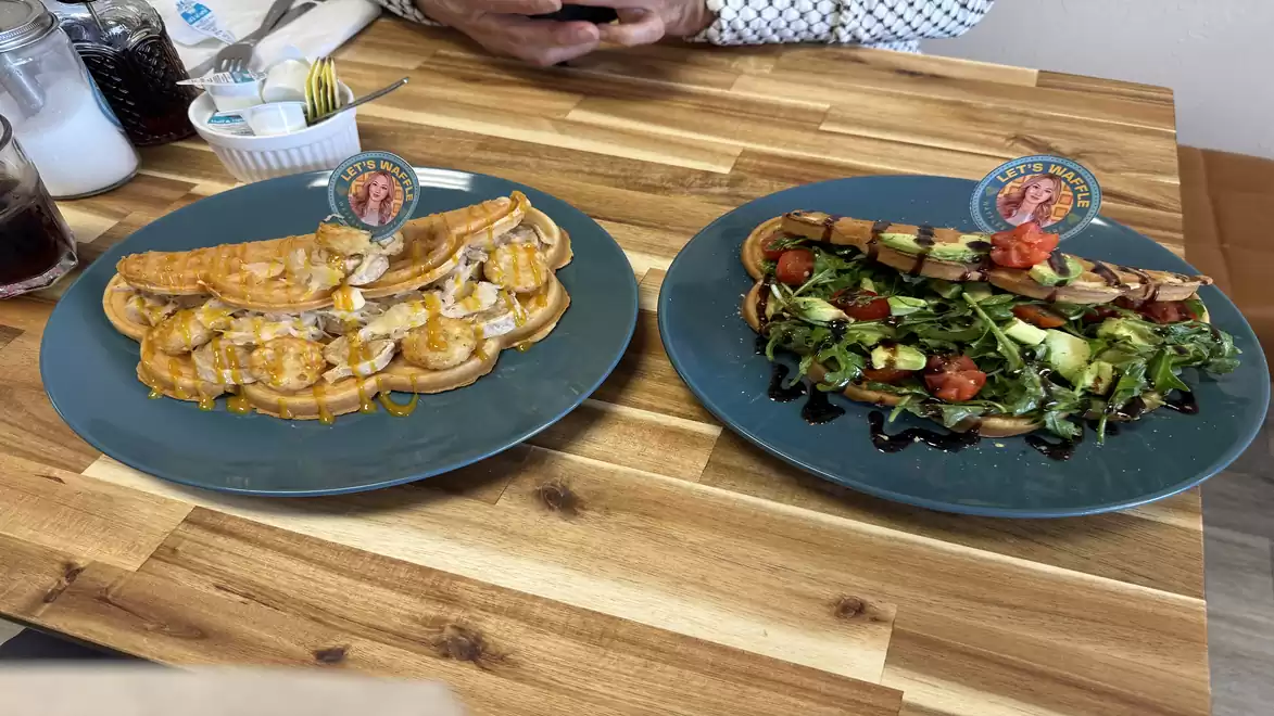 Two plates of delicious food on a wooden on a wooden table. On the left a plate with filled waffle (German Love) and a mustard sauce on top. mustard sauce, on the right a plate with the waffleAvocado Love with salad, avocado and balsamic vinegar.