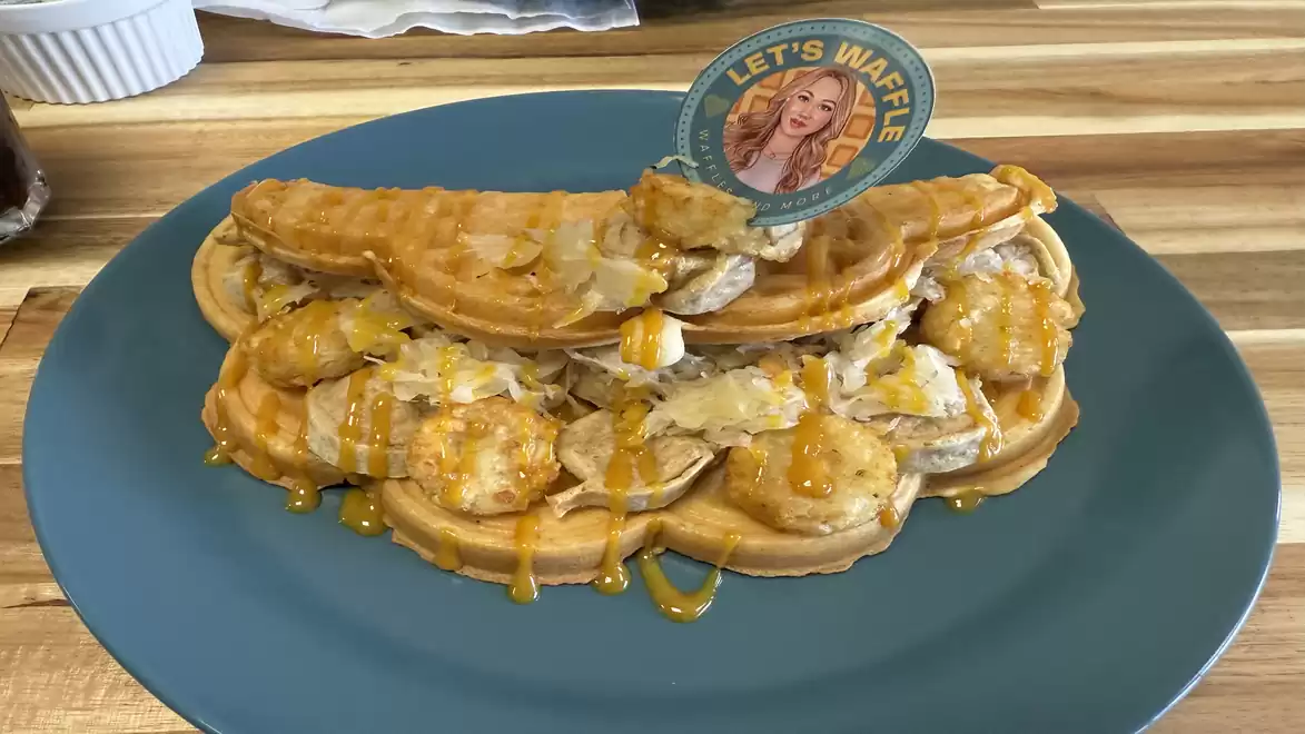 A plate of savory filled waffles (German Love), topped with slices of bratwurst, hash browns and mustard sauce, served on a blue plate.