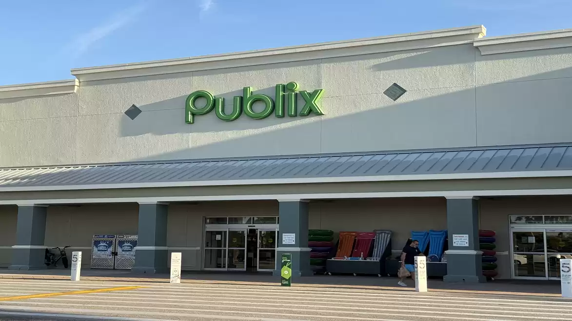 Entrance of a Publix supermarket with the green logo on the facade and several shopping carts in front.