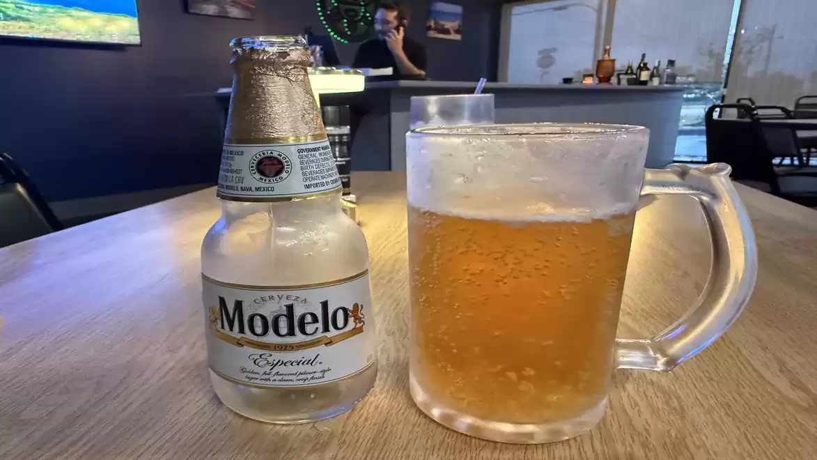 A bottle of Modelo Especial beer and a filled beer glass on a wooden table in a bar.