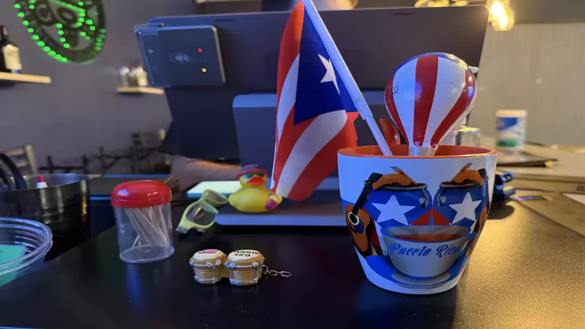 A cup with the design of the Puerto Rico flag sits on a table, surrounded by small jars and a rubber duck.