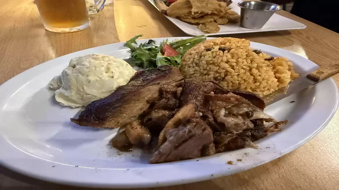 A plate with grilled meat, served with rice and a scoop of mashed potatoes, garnished with a small salad. A beer glass is visible in the background.