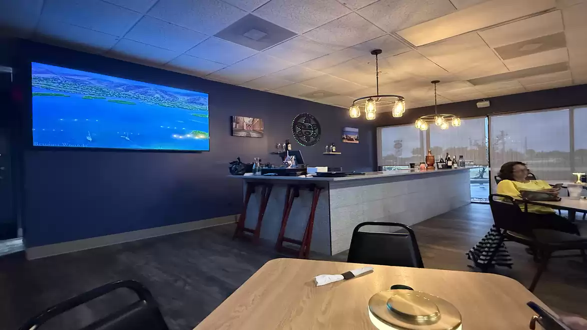 A modern Restaurant with blue walls and large windows. In the background, there's a counter and several tables. A large screen with a nature image hangs on the wall.