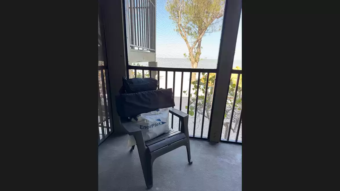 An empty chair on a balcony overlooking a tree and the sea in the background.