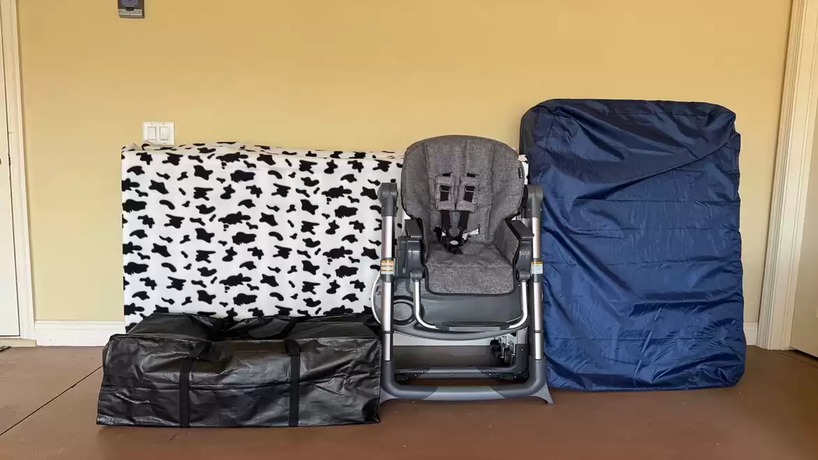 The image shows a child's high chair and several cushions and bags neatly lined up on a floor against a yellow wall.