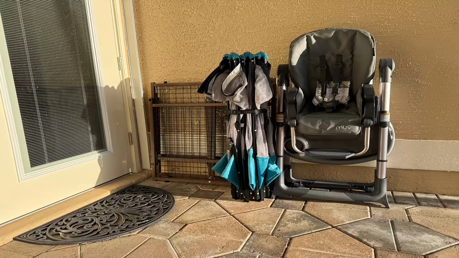 A foldable stroller and a high chair are placed on a patio next to a door.
