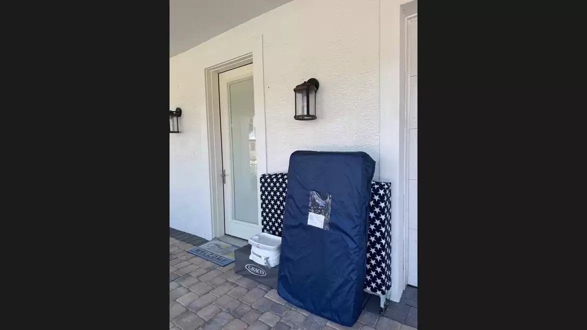 Front entrance of a house with blue mattresses and patterned curtains against the white wall.