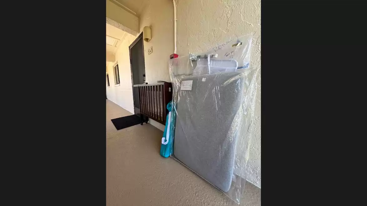 A large package wrapped in plastic, leaning against a wall in a building hallway. Next to it is a blue bag.