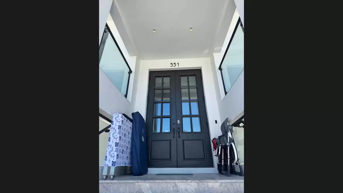 House entrance with modern black double doors and large side windows, accessed via a few steps with modern railings.