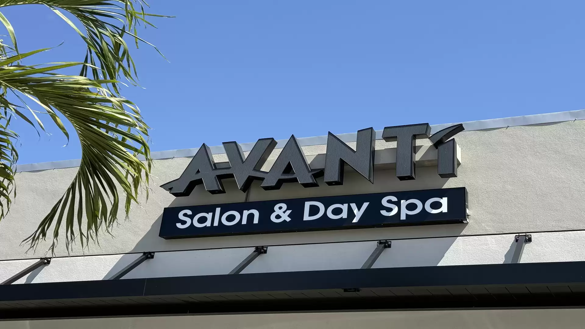 Exterior view of a building with the sign 'Avanti Salon & Day Spa' and a palm tree in the foreground.