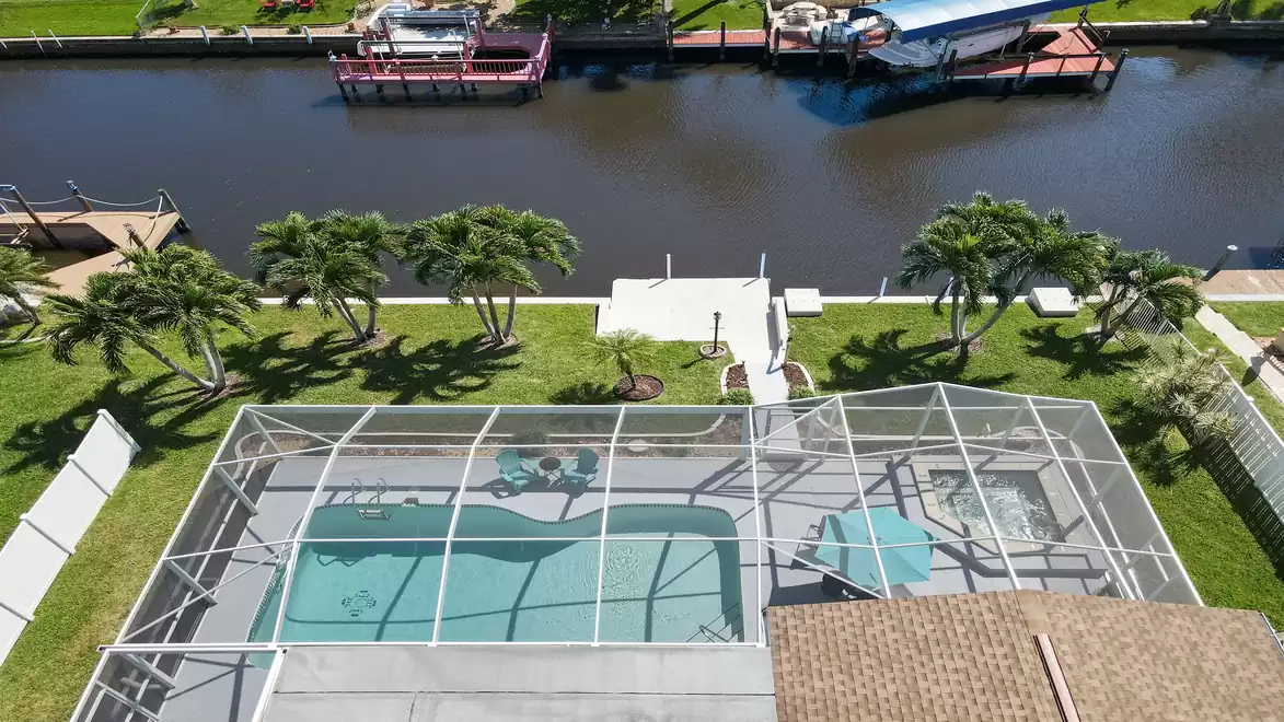 Villa Coral Sunshine - Aerial view of a screened swimming pool surrounded by palm trees next to a waterway with boat docks.